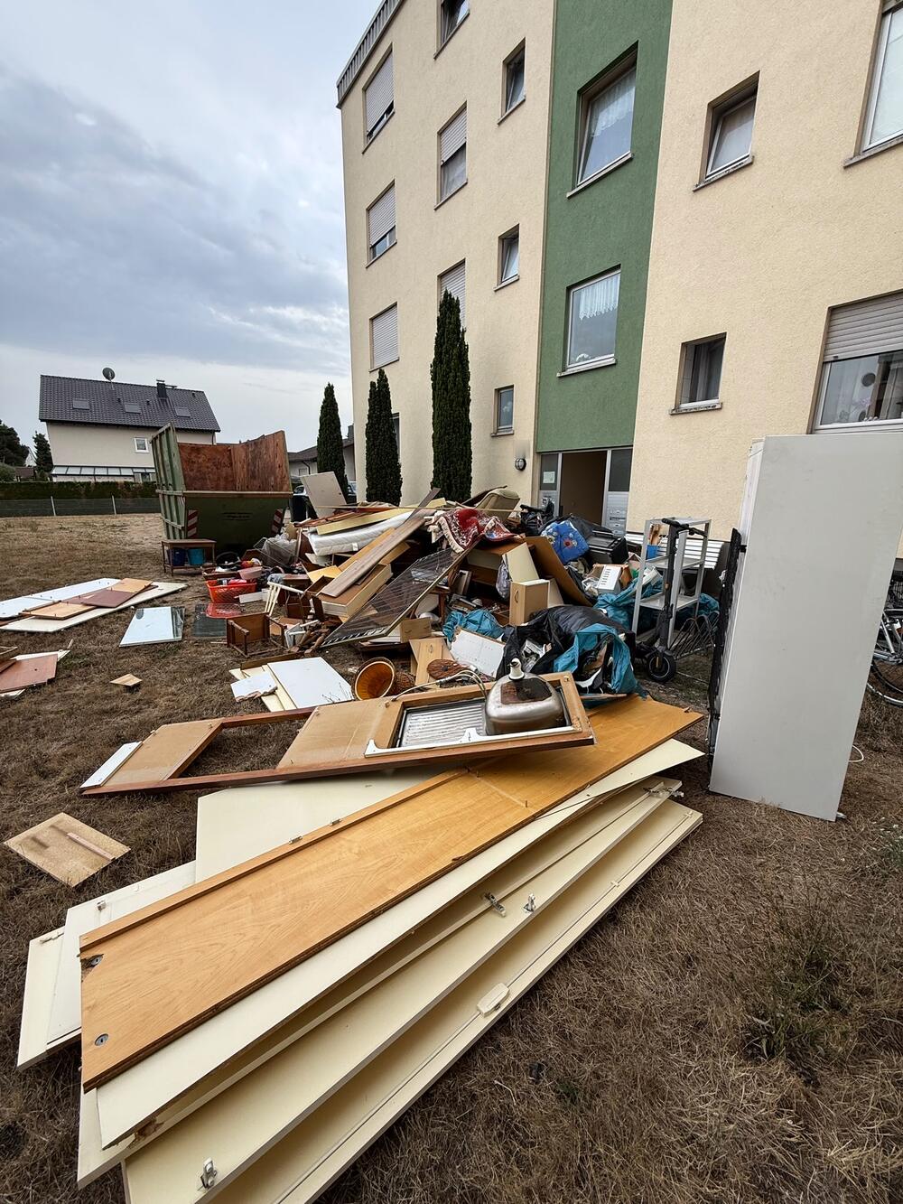 Ausgeräumte Möbel und Hausrat vor einem Mehrfamilienhaus, daneben ein Container